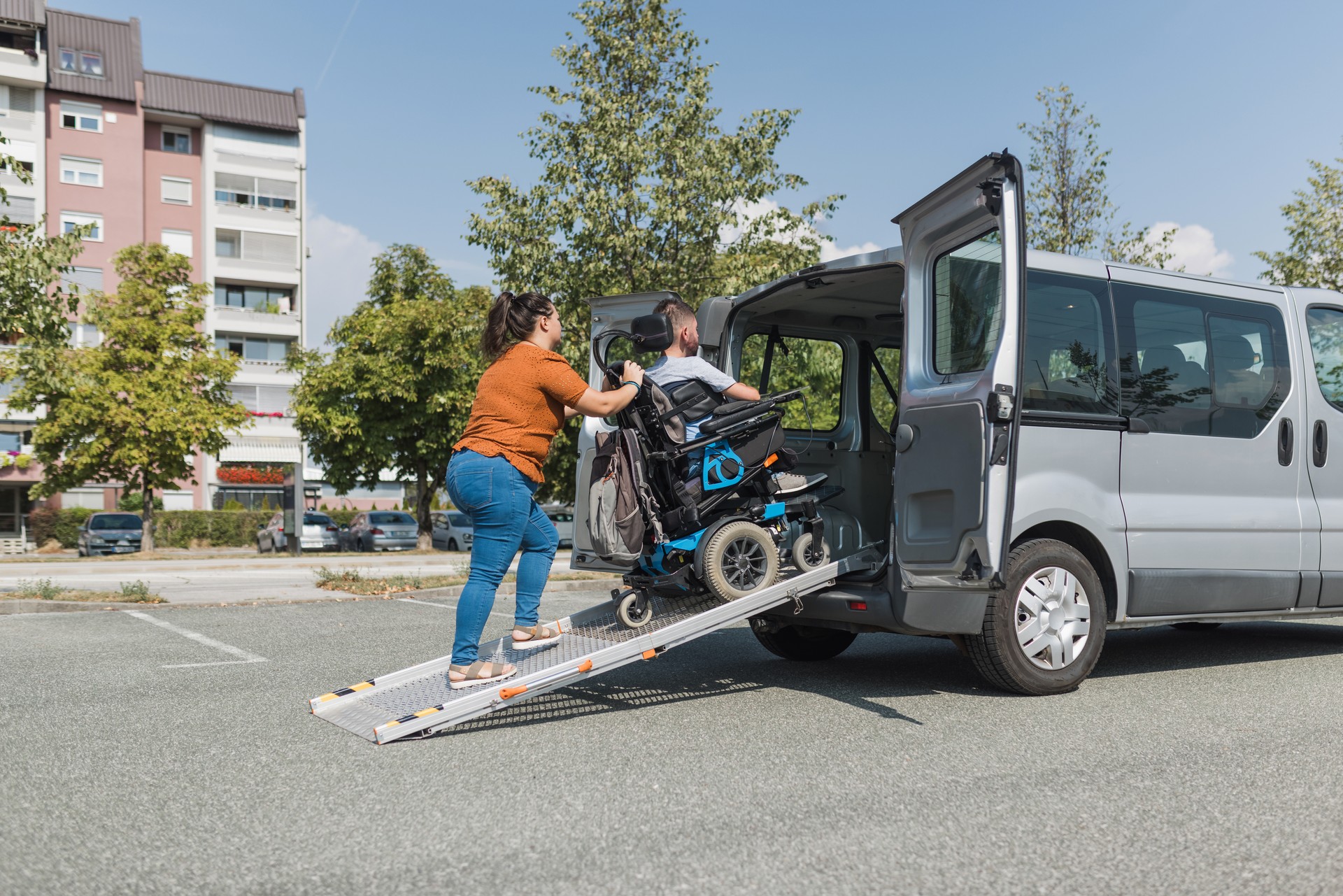 Assistant pushing a man in the wheelchair up an accessible car ramp